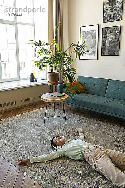 Glückliche Frau mit kabellosen Kopfhörern entspannt sich zu Hause auf dem Teppich