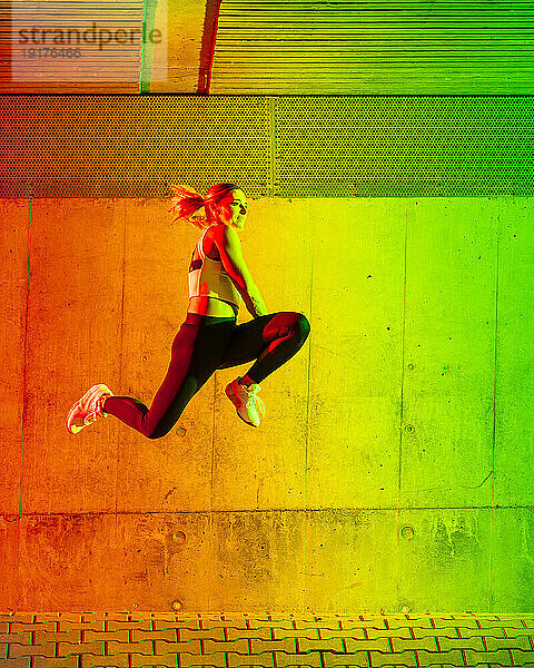 Aktive Frau springt vor neonfarbener Wand