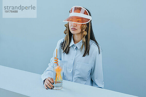 Thoughtful woman wearing sun visor with jellyfish and straw in glass at studio
