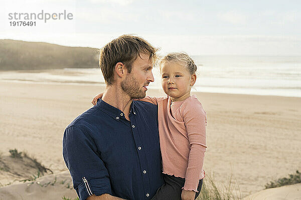 Lächelnder Mann trägt Tochter am Strand
