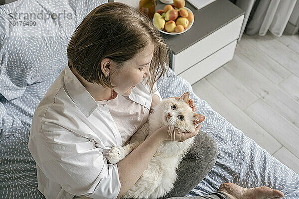 Happy woman playing with cat on bed at home