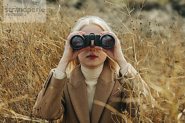 Blonde Frau schaut durch ein Fernglas im Feld