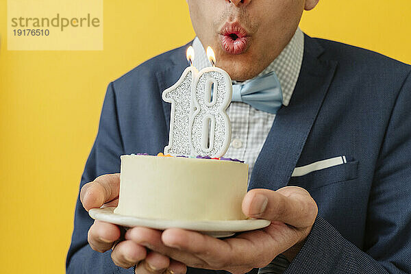 Mann bläst Kerze zum 18. Geburtstag auf Kuchen