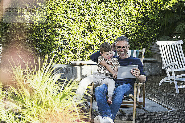 Glücklicher Mann und Junge mit Tablet-PC sitzen im Hinterhof