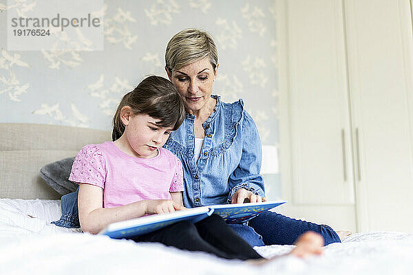 Tochter liest Bilderbuch mit Mutter im Schlafzimmer