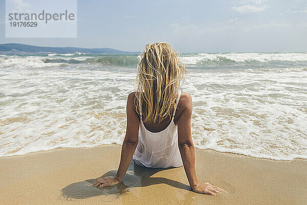 Blonde Frau sitzt auf Sand am Strand