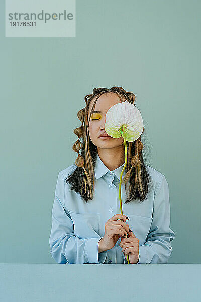 Young woman with eyes closed holding flower against blue background