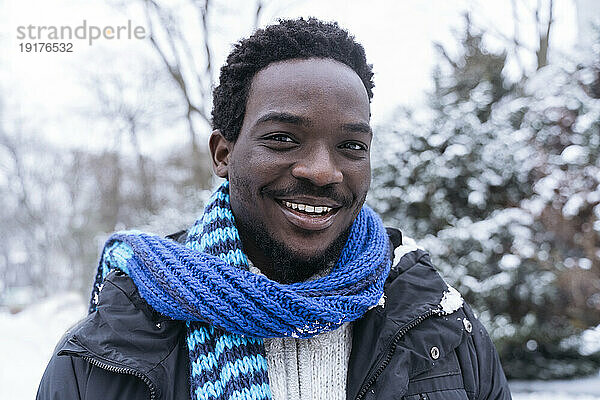 Lächelnder junger Mann mit blauem Schal im Winter