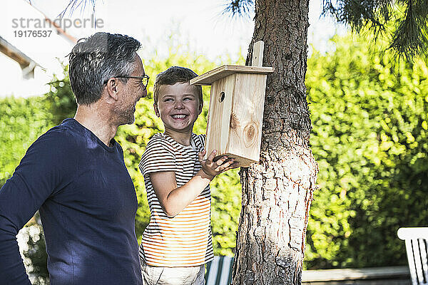 Glücklicher Junge repariert Vogelhaus am Baum von Großvater im Hinterhof