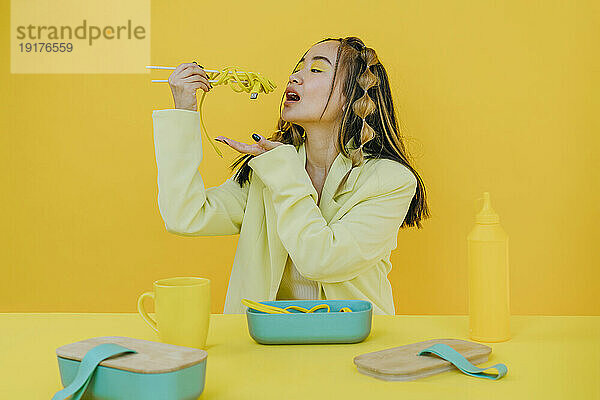 Junge Frau isst verkabelte Nudeln vor gelbem Hintergrund