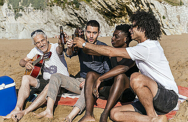 Multiethnische Freunde stoßen im Urlaub am Strand auf Bierflaschen an
