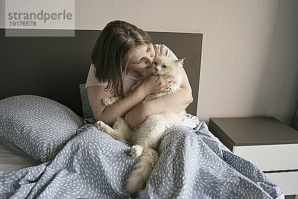 Frau küsst und streichelt Katze zu Hause im Bett