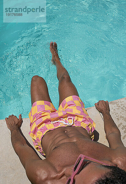 Junger Mann sitzt an einem sonnigen Tag am Pool