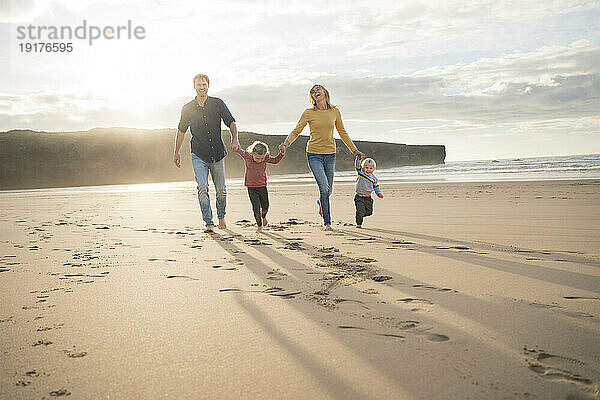 Glückliche Familie hält Händchen und geht am Strand spazieren