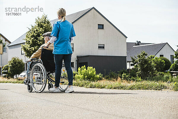 Gesundheitshelfer schiebt älteren Mann im Rollstuhl
