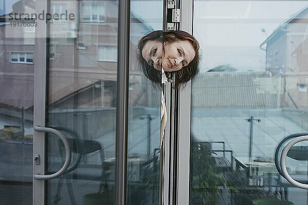 Lächelnde Geschäftsfrau  die aus der Glastür späht