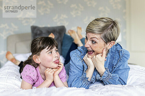 Fröhliche Mutter und Tochter machen Gesichtsausdruck auf dem Bett liegend