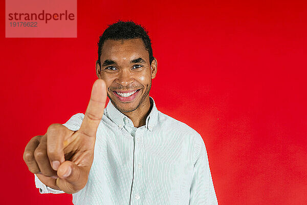 Lächelnder Mann zeigt mit dem Zeigefinger vor rotem Hintergrund