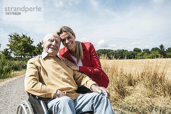 Lächelnde Frau mit älterem Mann  der an einem sonnigen Tag im Rollstuhl sitzt