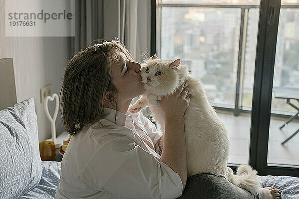 Junge Frau küsst Katze zu Hause im Bett