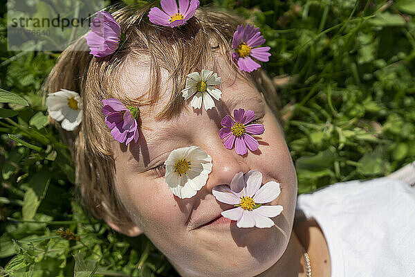 Lächelnder Junge mit Blumen im Gesicht an einem sonnigen Tag