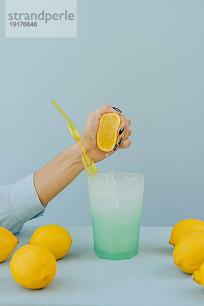 Hand of woman squeezing lemon in cocktail glass on table