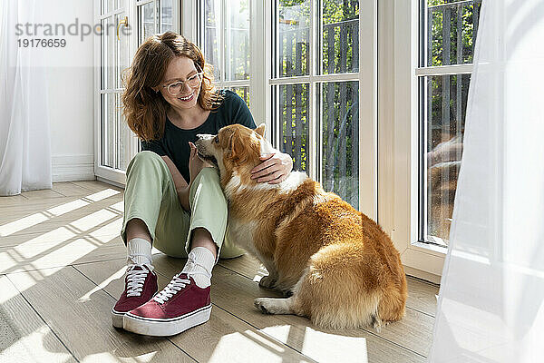 Smiling woman stroking Welsh Corgi dog sitting at home