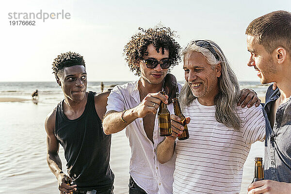Fröhliche multiethnische Freunde  die im Urlaub Bier am Strand trinken