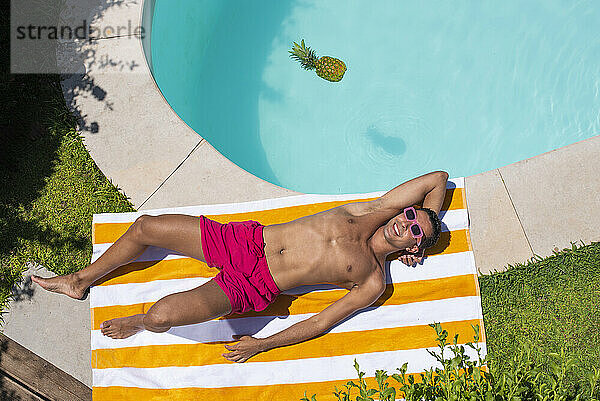 Glücklicher Mann entspannt sich auf einem gestreiften Handtuch am Pool