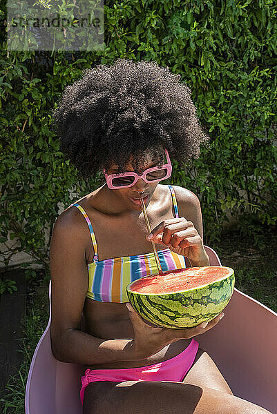 Junge Frau trinkt an einem sonnigen Tag Wassermelonensaft mit Strohhalm