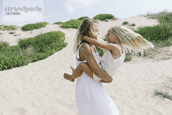 Lächelnde Mutter  die an einem sonnigen Tag Spaß mit ihrer Tochter am Strand hat