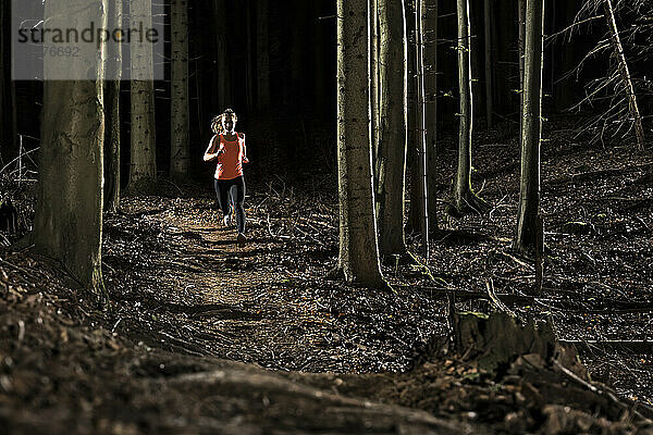 Junger Athlet läuft inmitten von Baumstämmen im Wald