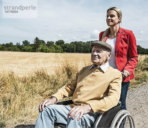 Frau schiebt an sonnigem Tag einen älteren Mann  der im Rollstuhl sitzt