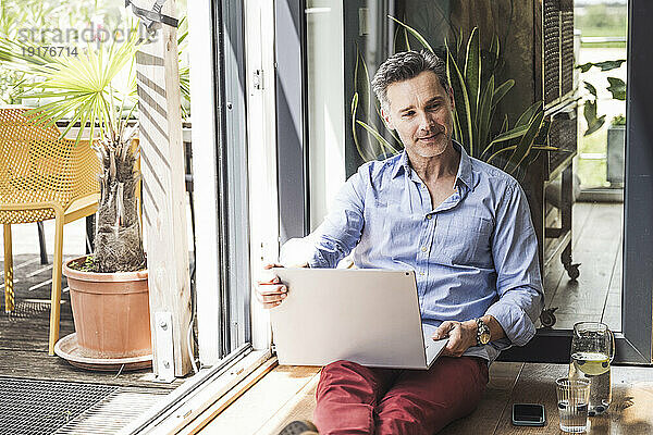 Porträt eines Mannes mit Laptop am offenen Balkon