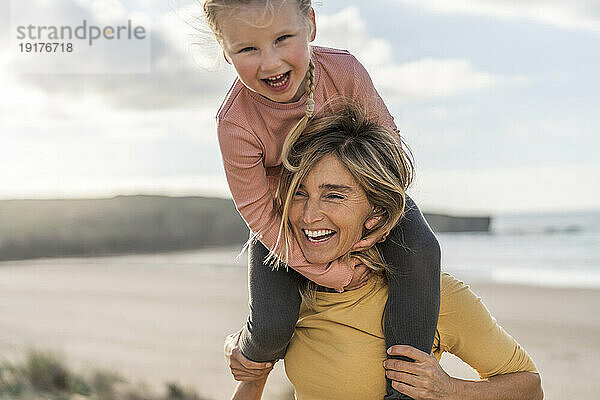 Glückliche Mutter trägt Tochter auf Schultern am Strand