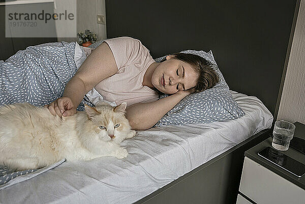 Junge Frau schläft zu Hause neben Katze im Bett