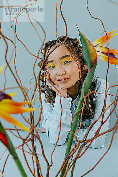 Young woman with hand on chin seen through multi colored branches in studio