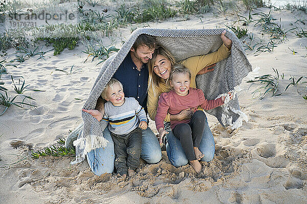 Happy family under blanket on sand at beach