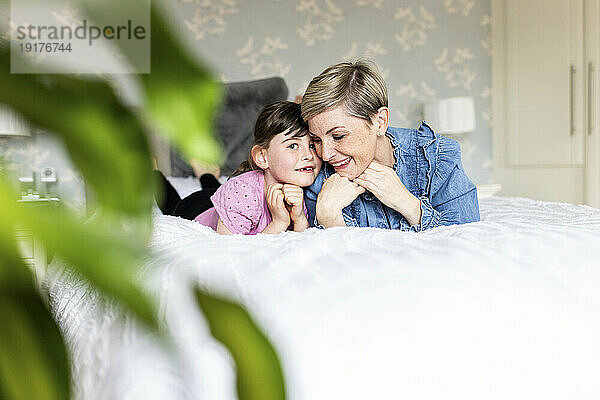 Mother and daughter with hands on chins lying in bedroom