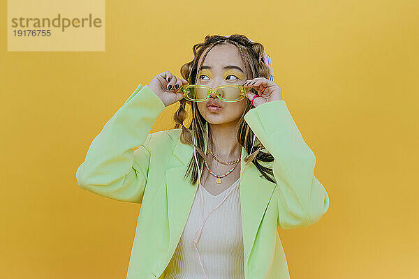 Young woman wearing sunglasses and puckering against yellow background in studio