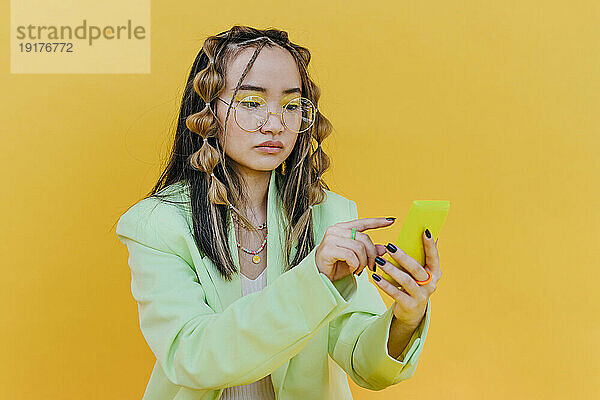 Junge Frau mit Sonnenbrille benutzt Mobiltelefon im Studio