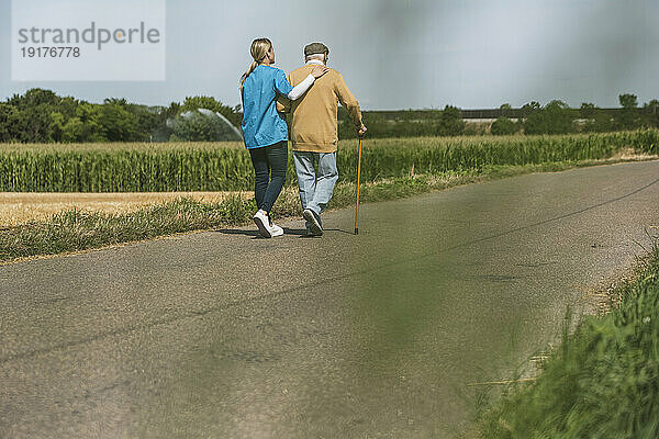 Gesundheitshelfer geht an sonnigem Tag mit älterem Mann auf der Straße spazieren