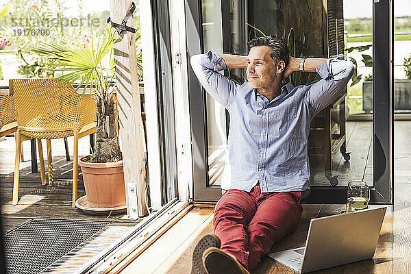 Porträt eines Mannes  der sich mit Laptop auf dem offenen Balkon entspannt