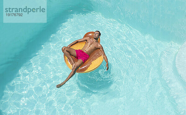 Junger Mann entspannt sich auf aufblasbarem Schwimmkörper im Pool