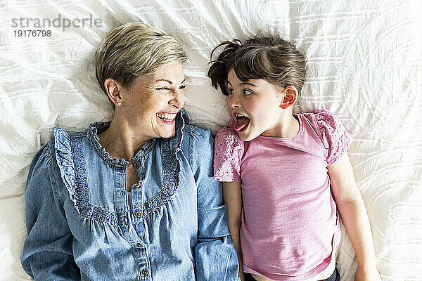 Girl sticking out tongue and lying down by mother at home