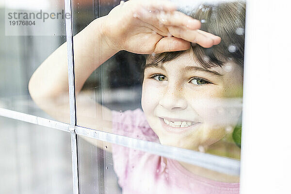 Lächelndes Mädchen  das durch das Fenster schaut