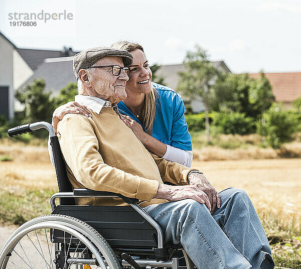 Lächelnde Krankenschwester umarmt älteren Mann im Rollstuhl