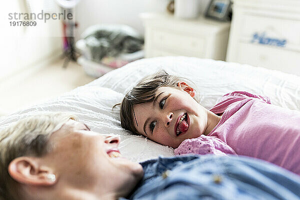 Girl sticking out tongue and lying down by mother in bedroom