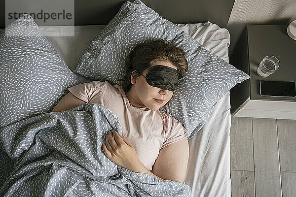 Frau mit Augenmaske schläft zu Hause im Bett