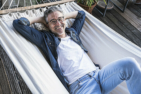 Happy mature man lying down in hammock at home